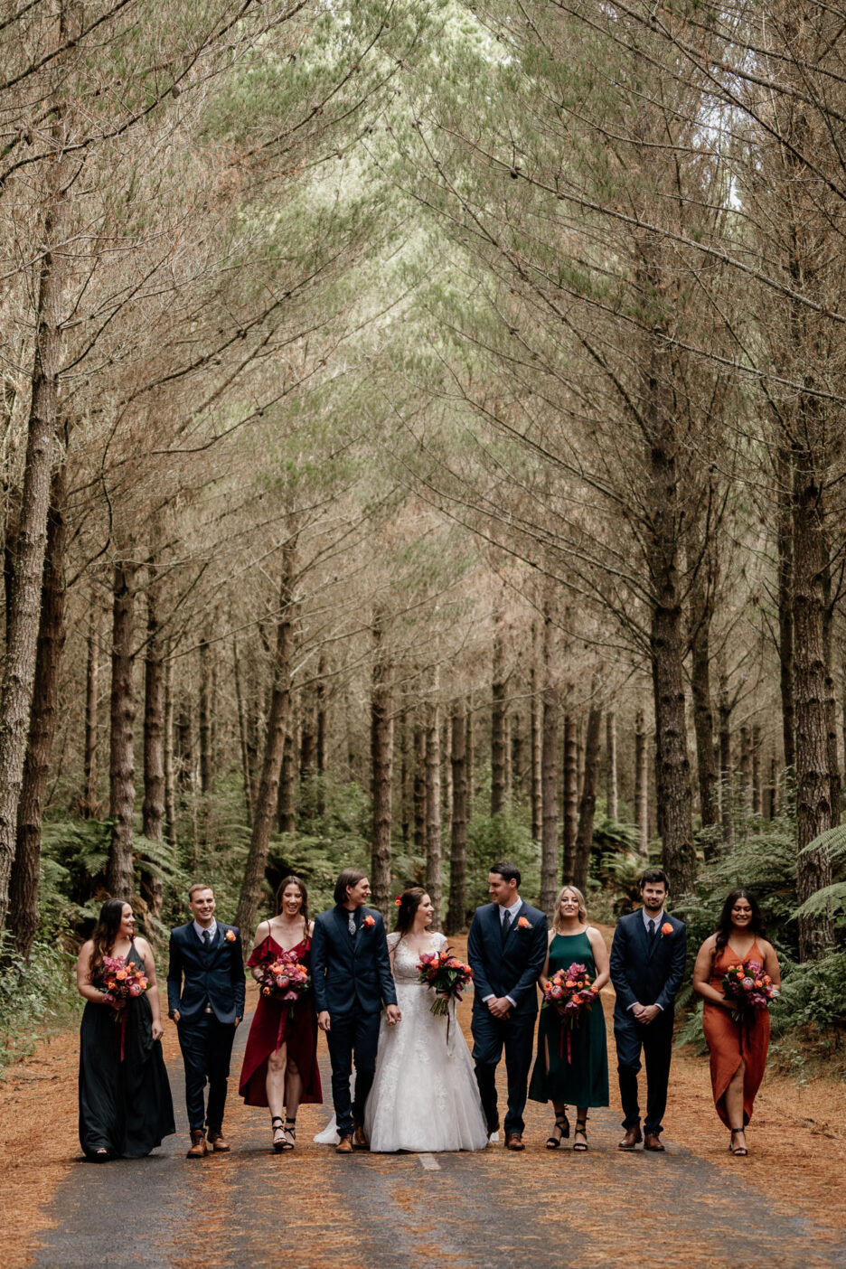Autumn wedding in New Zealand Rotorua forest with winter colours bridal party walking on road
