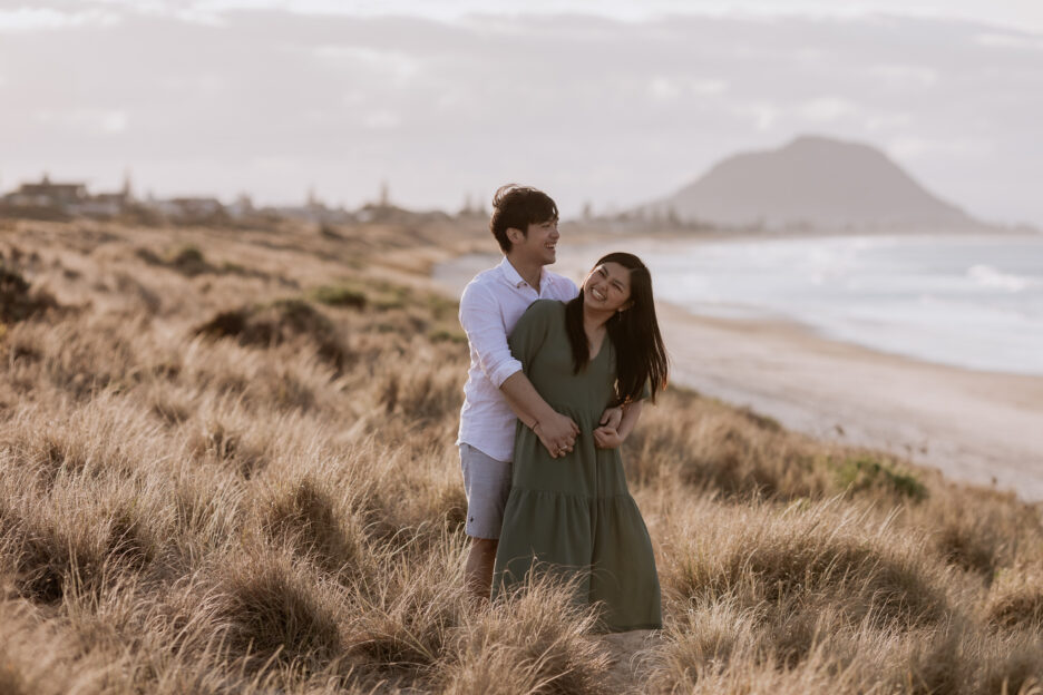 Laughing engagement photos of couple in Tauranga beach sand dunes