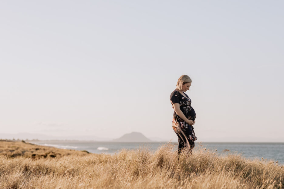 Maternity photo with Mom in sanddunes with soft tussocks around her, with the beach in the background