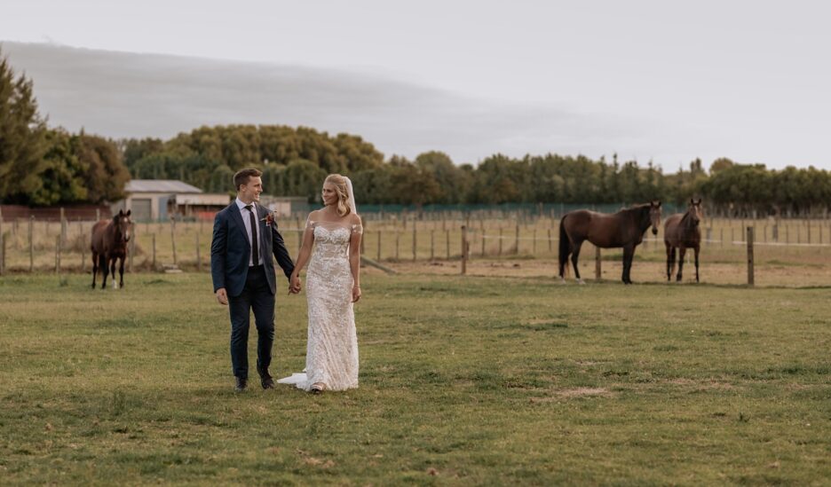 Bride and groom walking on farm with horses