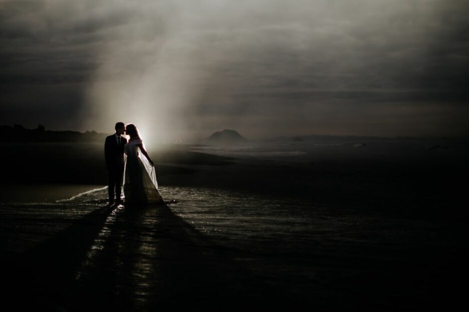 Bride and groom kissing flash shot on New Zealand beach of elopement photography