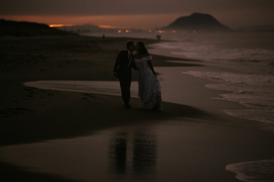 Moody wedding photo of bride and groom walking on the beach