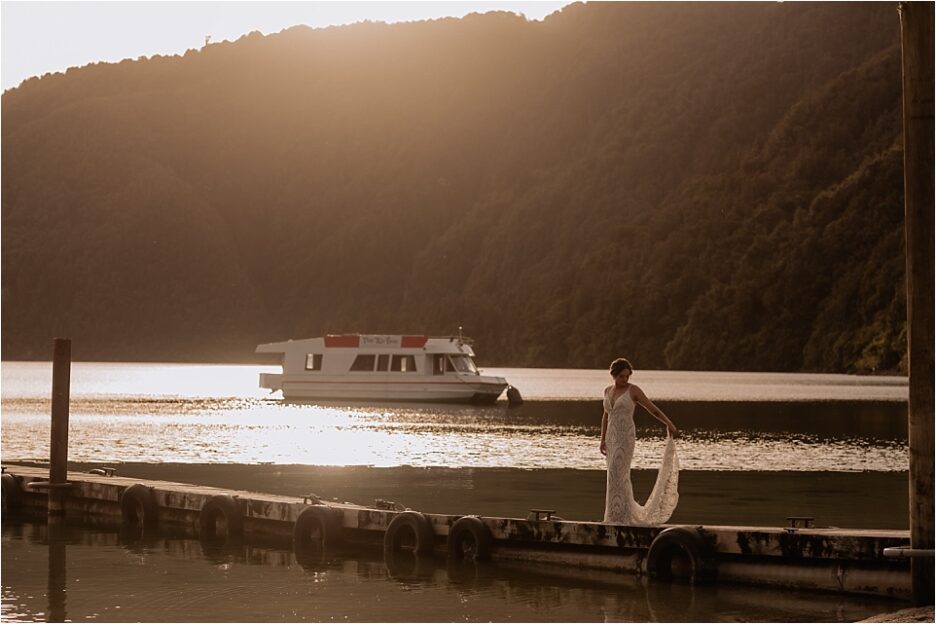 Bride on pier at golden hour with sun setting behind the hills