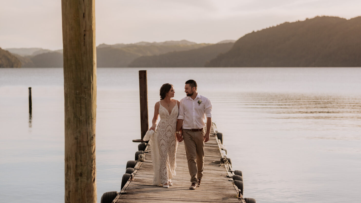 Bridal couple walking on pier at Lake Okataina golden skies