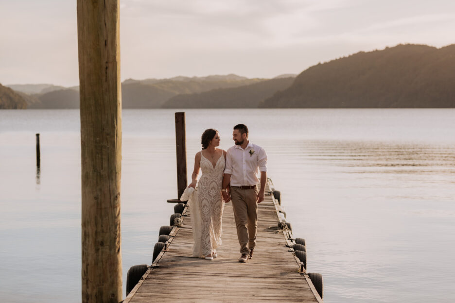 Bridal couple walking on pier at Lake Okataina golden skies