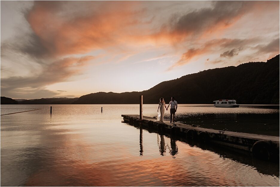 Sunset photo of bride and groom walking on pier at Lake Okataina