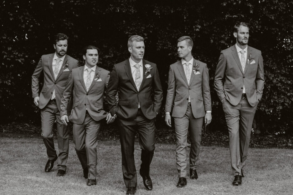 Groom with groomsmen walking black and white photo