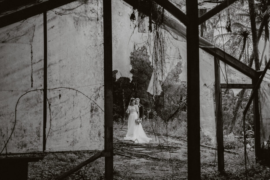 Moody image of bride and groom in abandoned rustic glass house