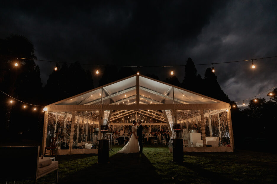 Evening photos of wedding couple in front of marquee at back yard wedding at night time