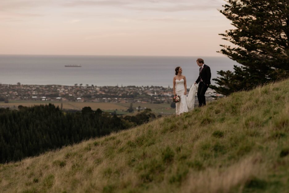 Bride and groom walking high on hills with ocean behind them