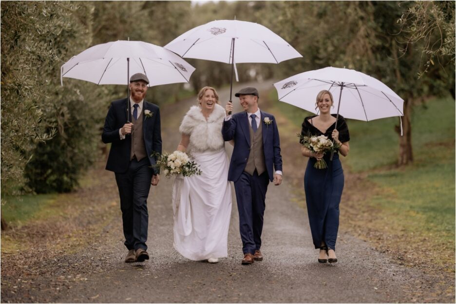 bridal party walking in the rain with umbrellas at Bracu New Zealand