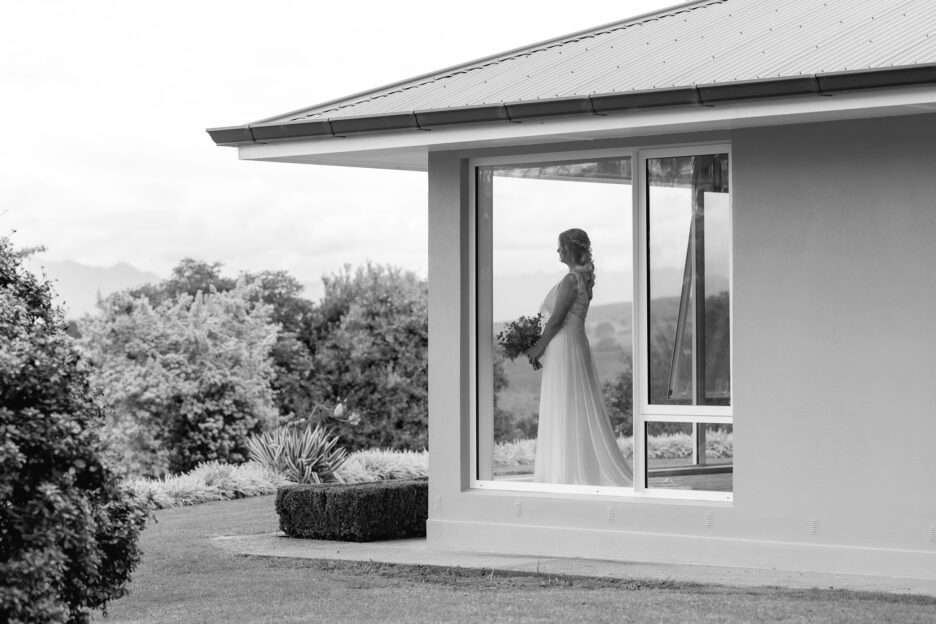 Bride in window of farm house overlooking ceremony area