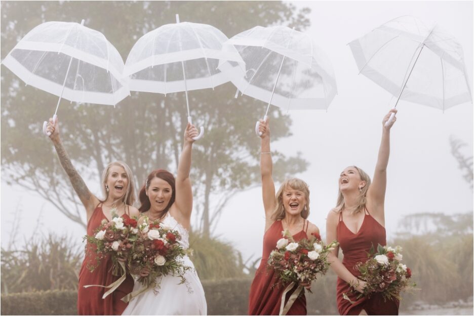 Party fun bride with bridesmaids holding up umbrellas in wine dresses.