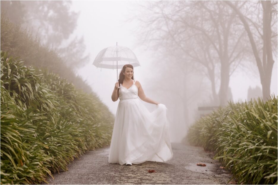 Bride walking on drive with umbrella in the clouds