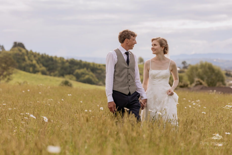 bride and groom in field of daisies walking looking at eachother