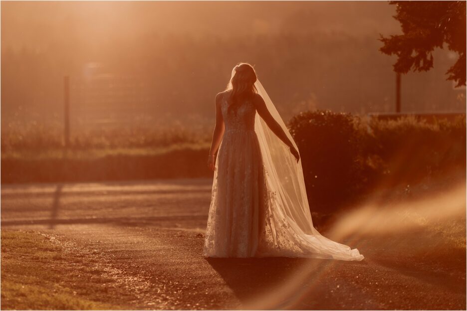 Bride holds out veil in golden light as sunshine shines through