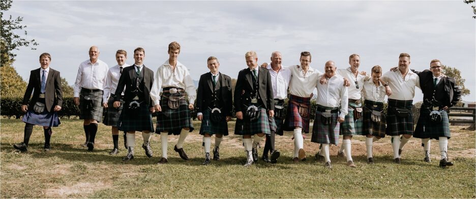 Guests and groomsmen in New Zealand all wearing kilts lined up walking