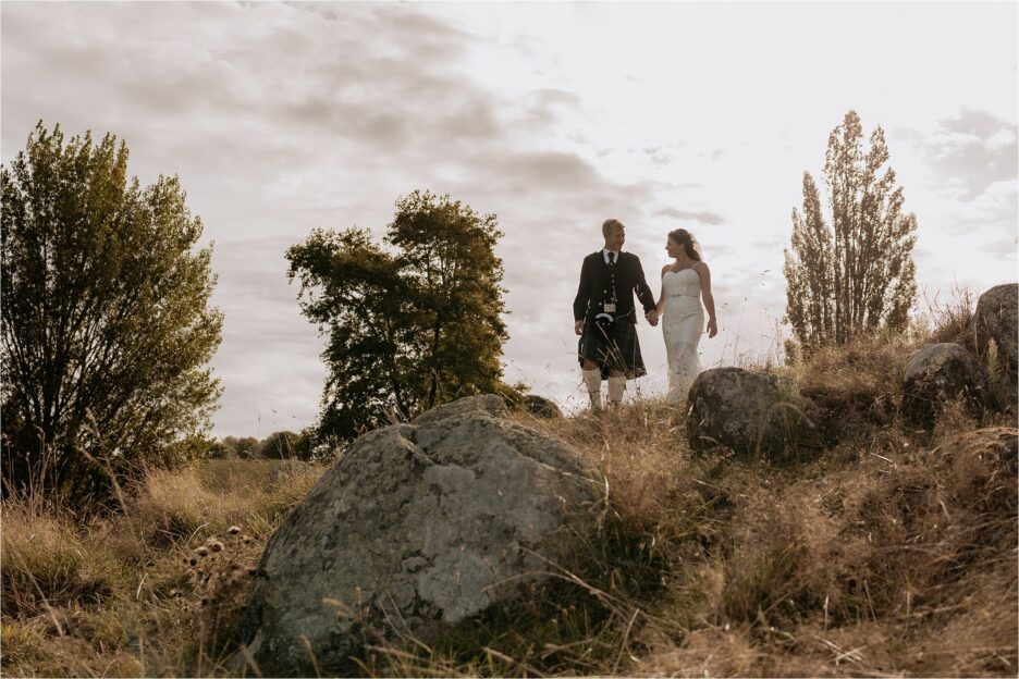 bride and groom holding hands on hill above rocks