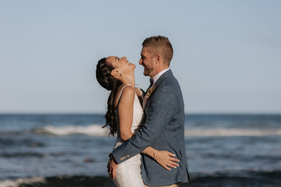Coromandel wedding photo at Orua beach house on rocks bride throws head back laughing