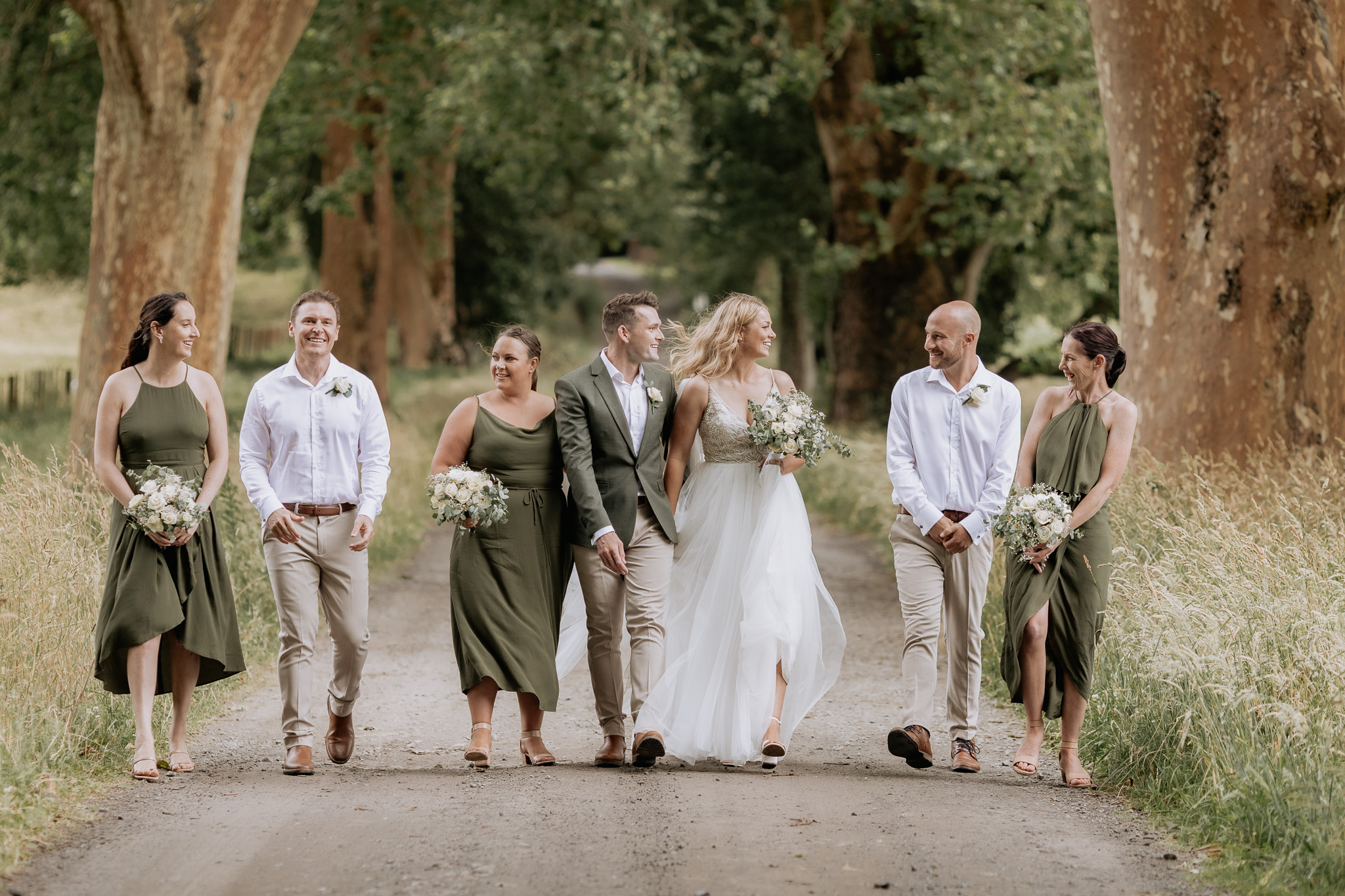 Olive green wedding party walking laughing driveway Longfords estate