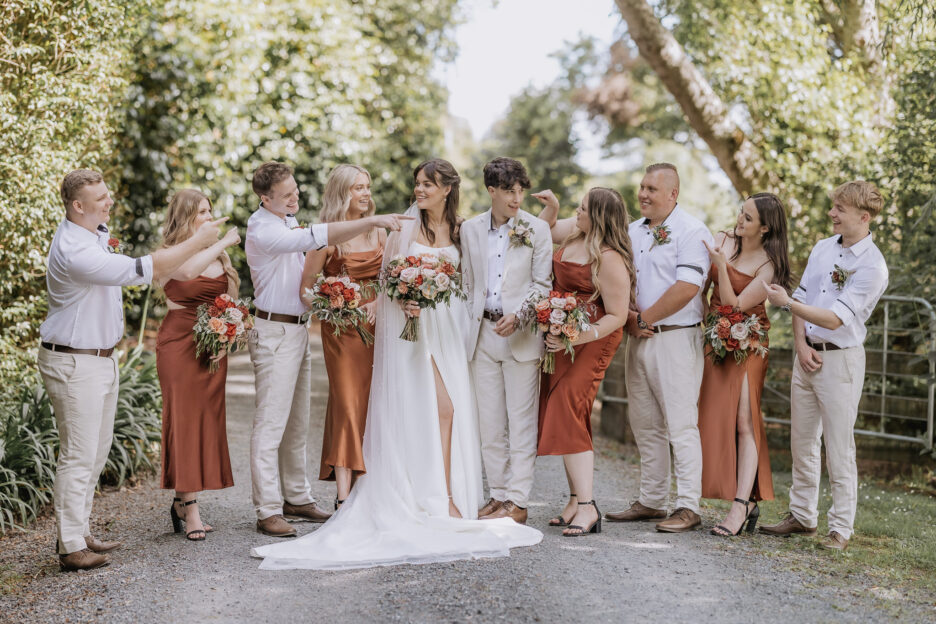 wedding party boys in linen suits and bridesmaids in rust brown dresses laughing