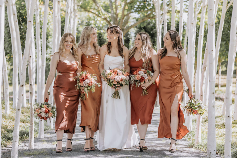 bride and orange bridesmaids walk in trees Ohaupo tree church garden wedding