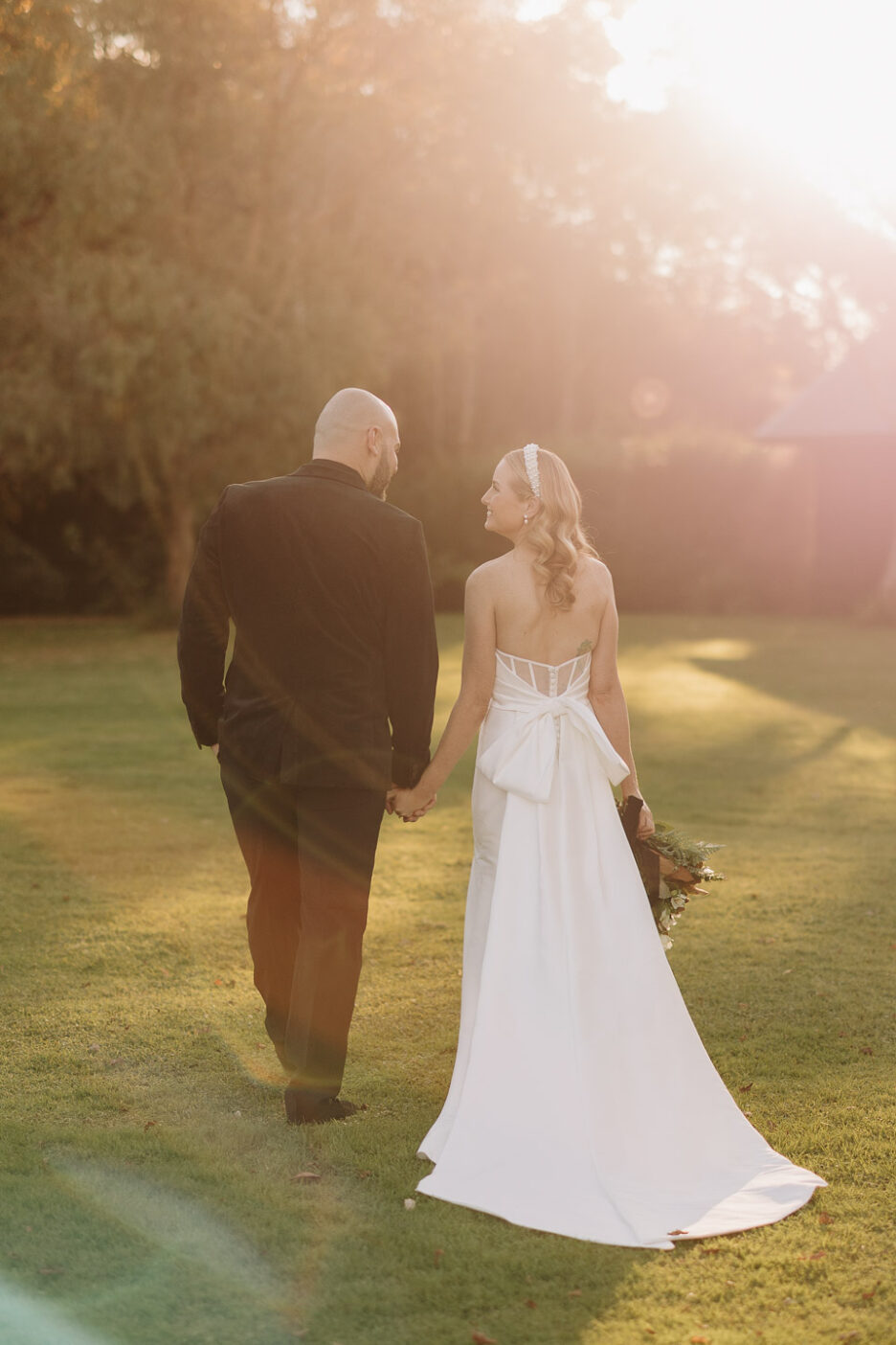 bride and groom walk away sunlight skimming over trees at Black Walnut wedding venue