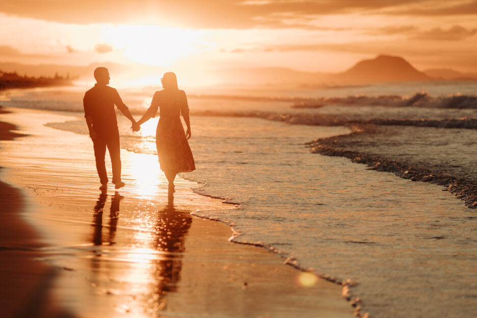 walking on beach holding hands at sunset Mount Maunganui