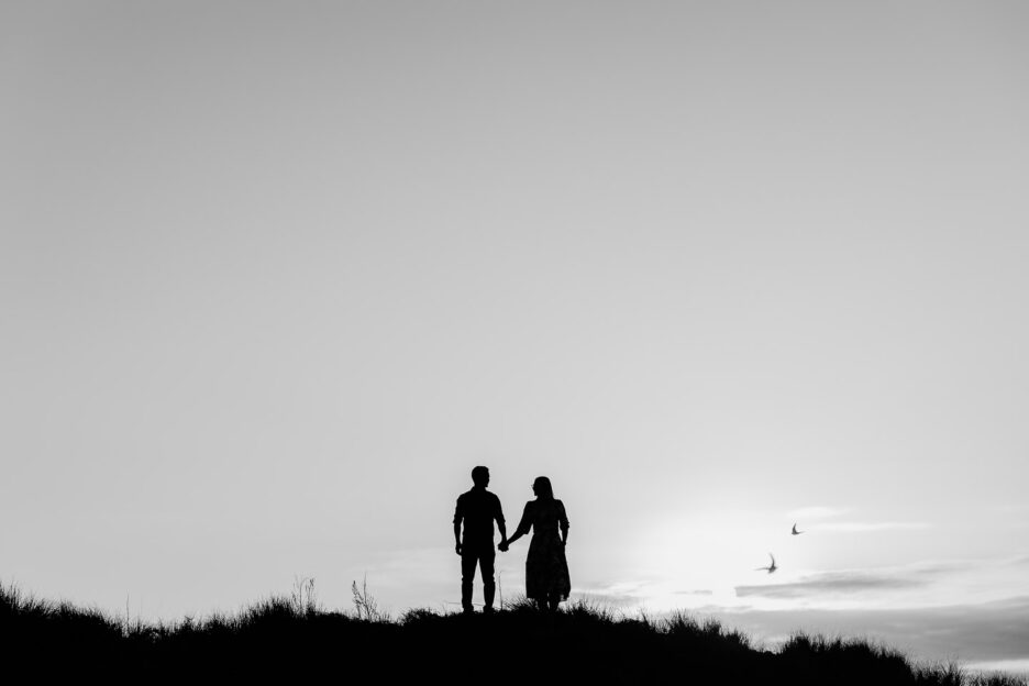 Couple standing top of sand dunes with birds flying beside them