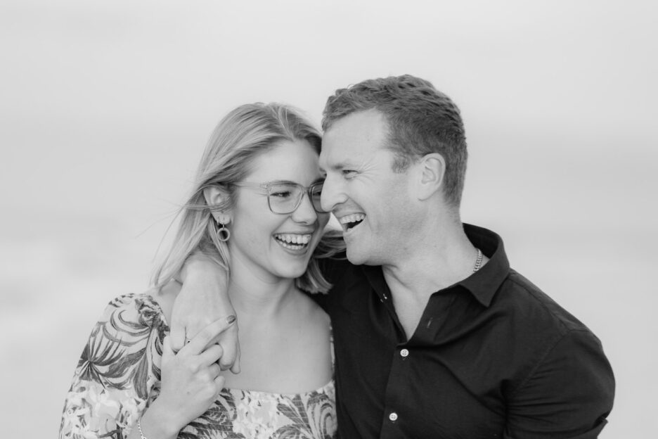 girl laughs at her fiance black and white candid photo during engagement shoot on Papamoa Beach by Tauranga wedding photographer pure images Photography