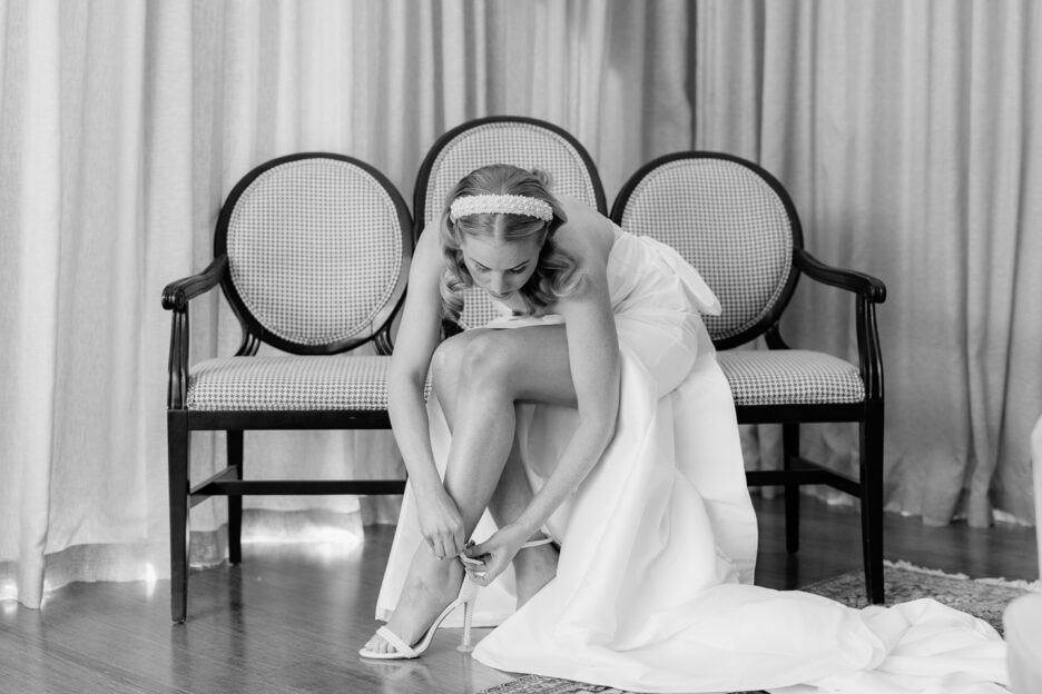 bride with pearl head band tying shoes