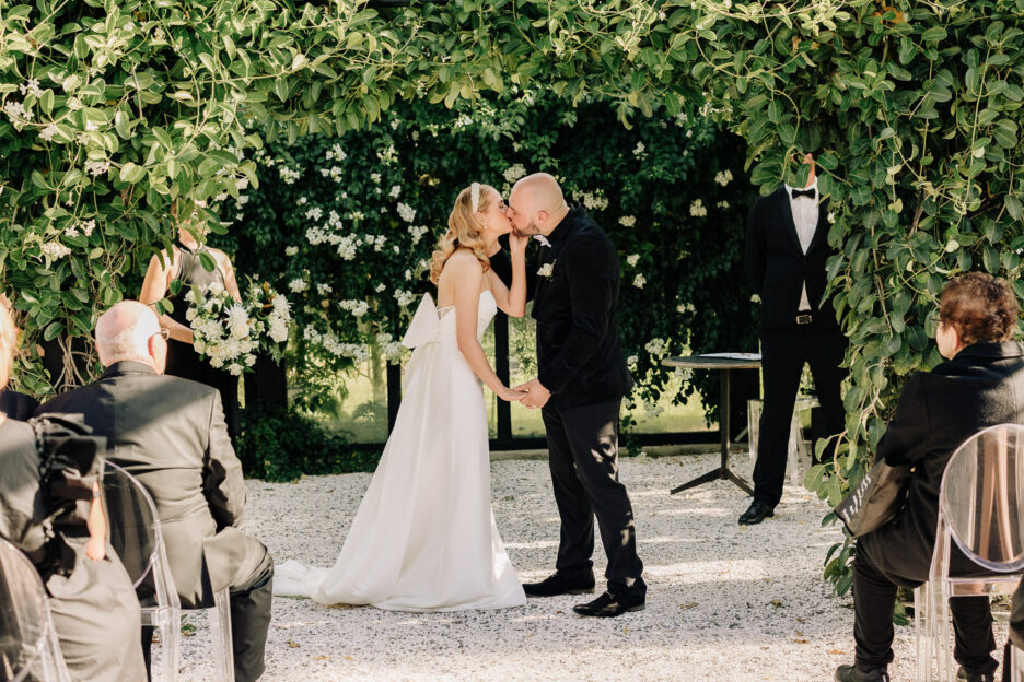 bride and groom first kiss under greenery in glass house Tauranga