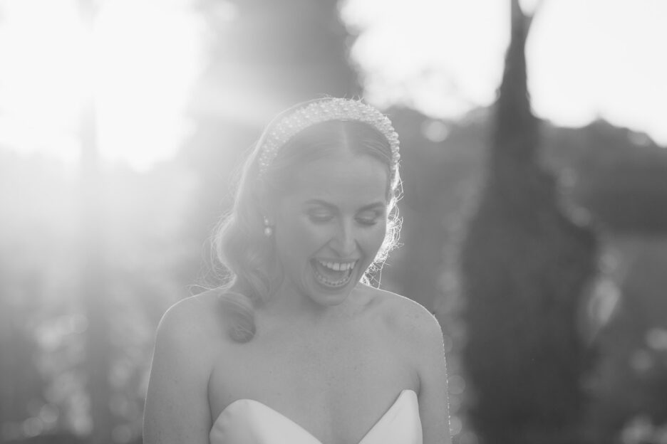 black and white image of bride laughing as sun flares behind