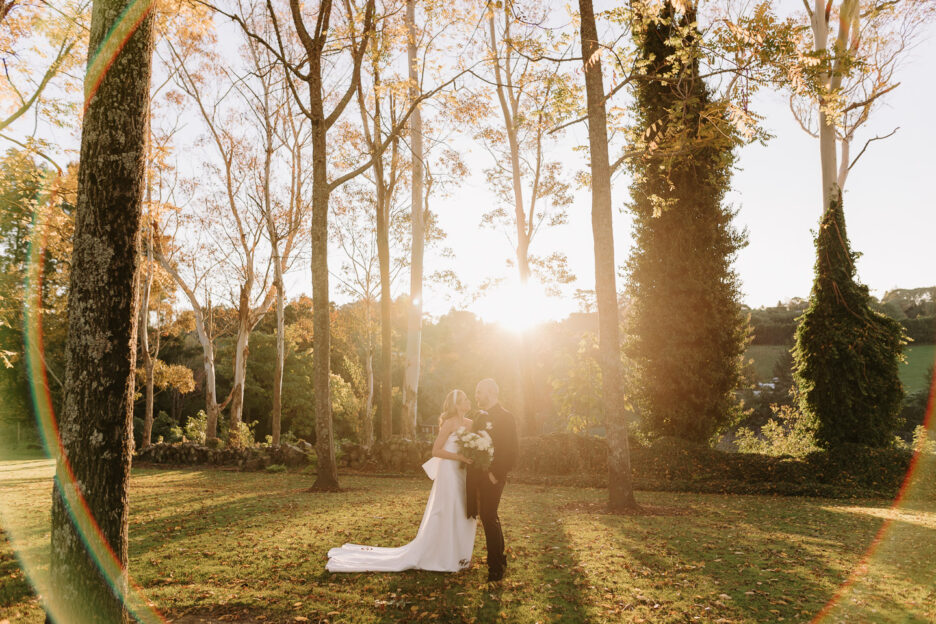 sun flare arounds a wedding couple during photos with golden light with trees behind them