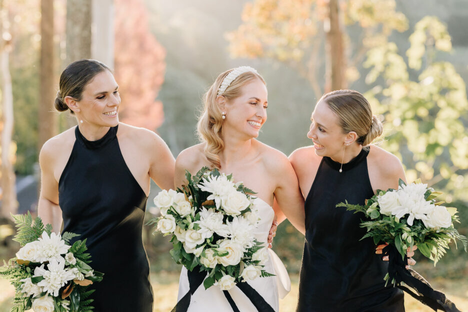 giggling bride with bridesmaids walk in golden light white and green bouquets