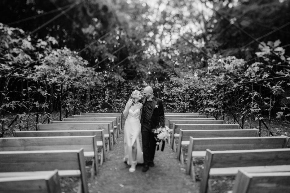 Black and white image of bride and groom walking down tree church aisle