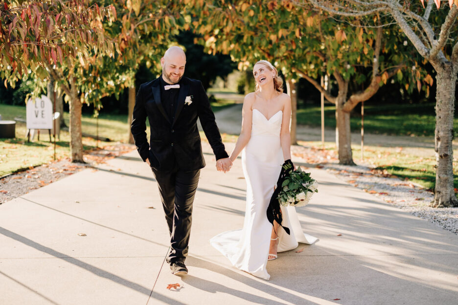 wedding photos as couple walk up driveway in between autumn trees