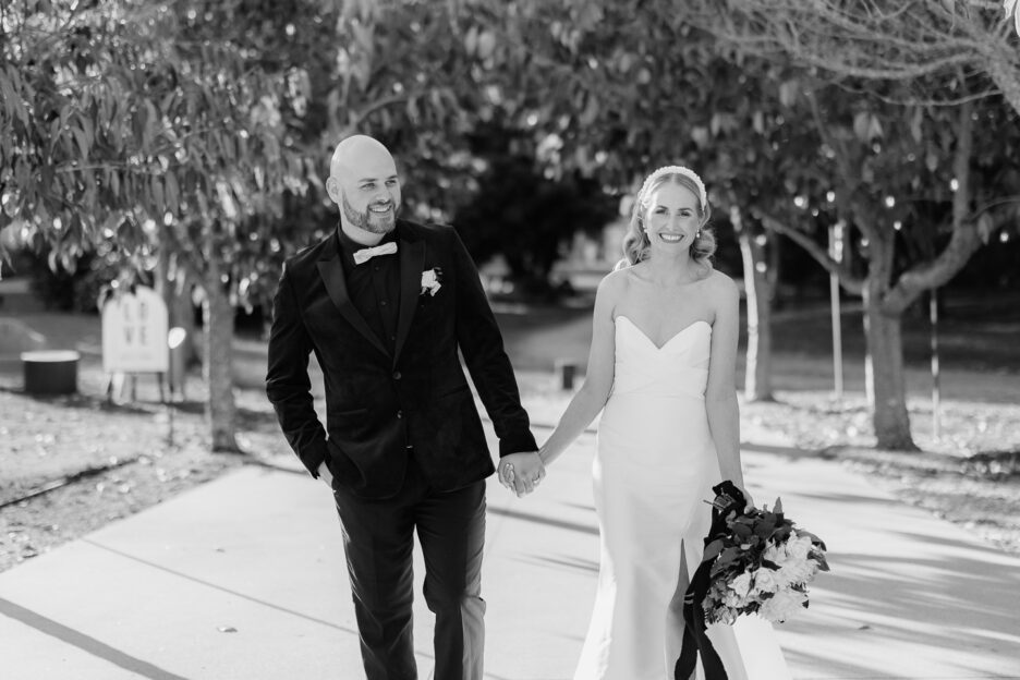 black and white photo of happy bride and groom walking down aisle of trees at black walnut wedding venue