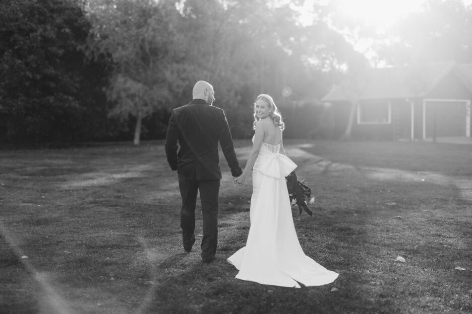 black and white image of bride looking over her shoulder walking away as sun sets