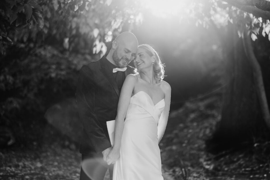 black and white photo of bride and groom cuddling in late light with sun flares