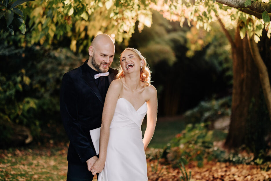 groom and bride laughing under autumn tree