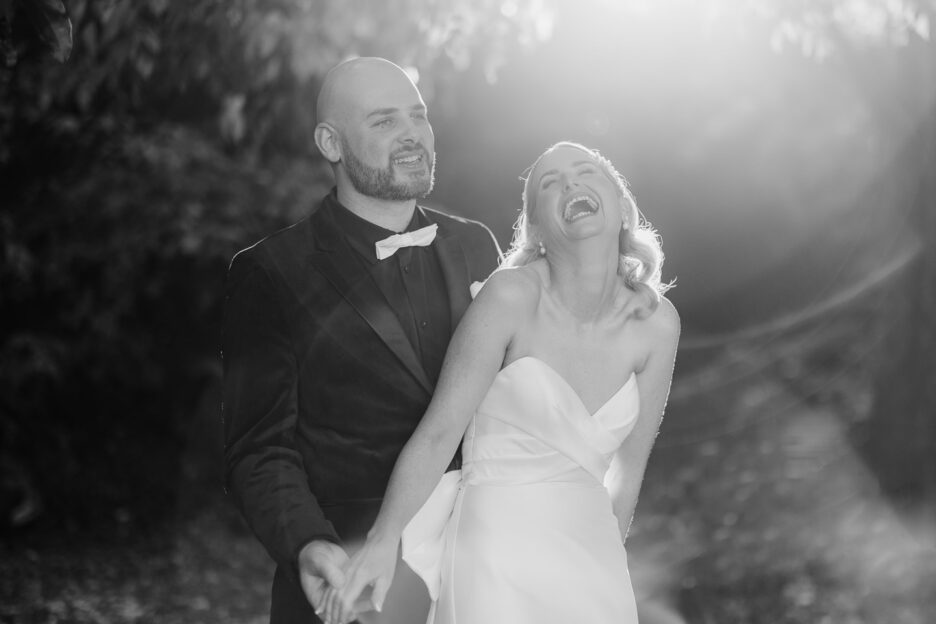 black and white photo of couple laughing as sun flare behind them