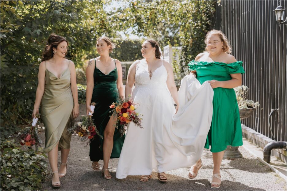 bride walks behind ebony vines with her bridesmaids all in different shades of green