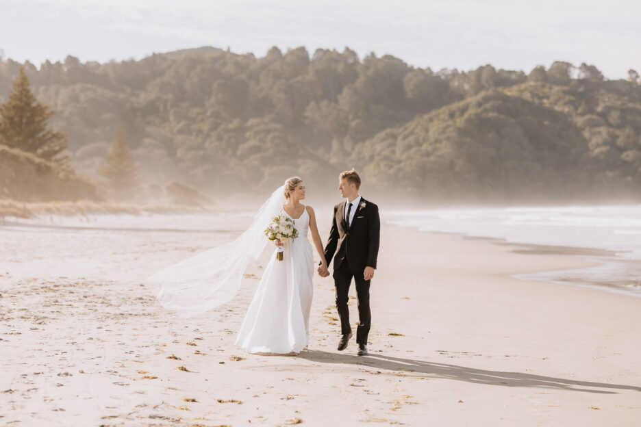 bride and groom walking waihi beach on sand