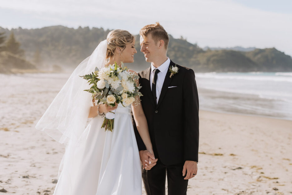 bride and groom looking at eachother on waihi beach in front of flat white cafe