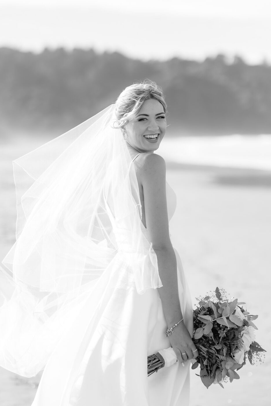 bride looks over her shoulder laughing on waihi beach