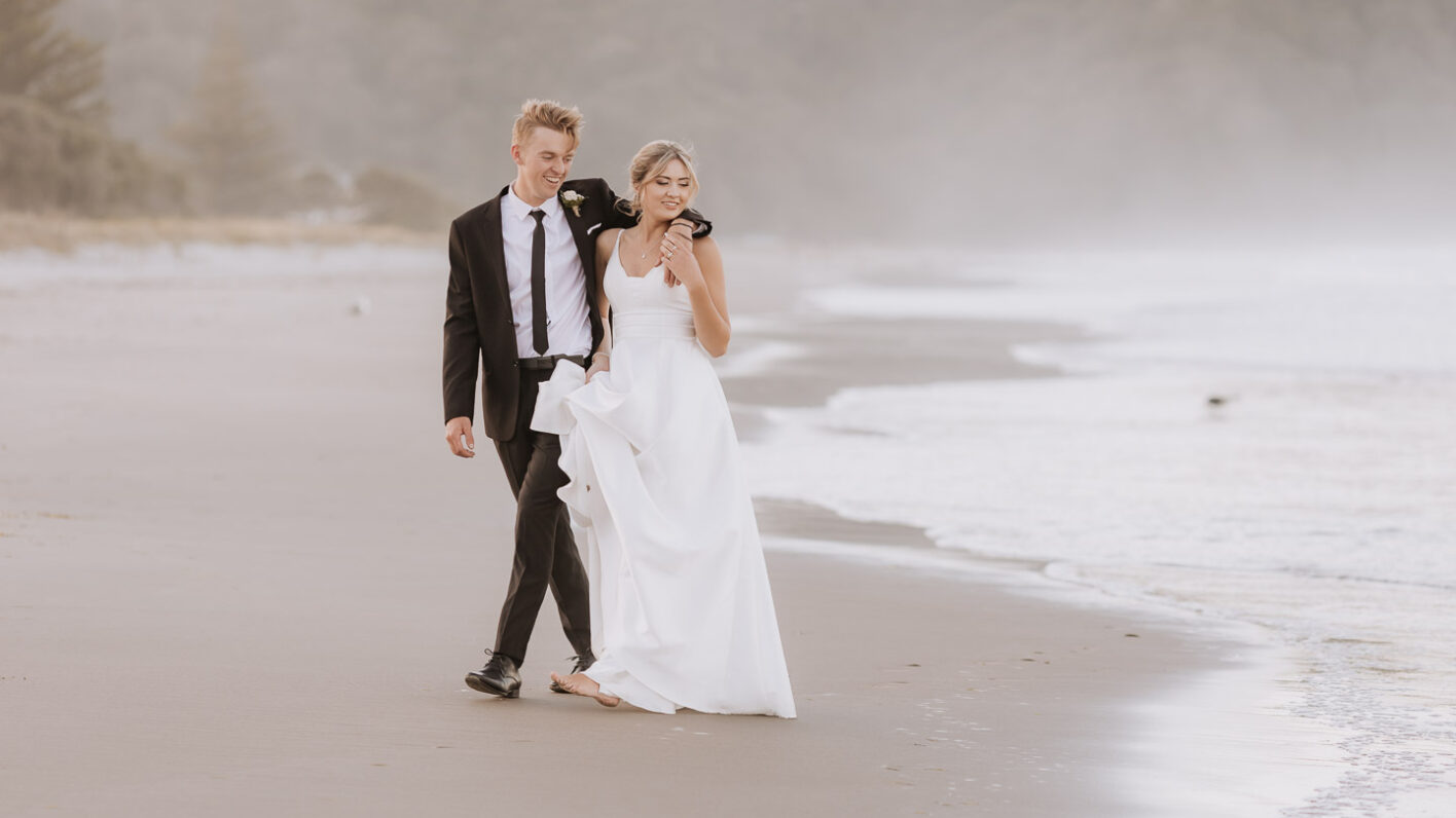 Wedding couple walking avoiding waves grooms arm around shoulder