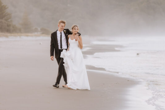 Wedding couple walking avoiding waves grooms arm around shoulder