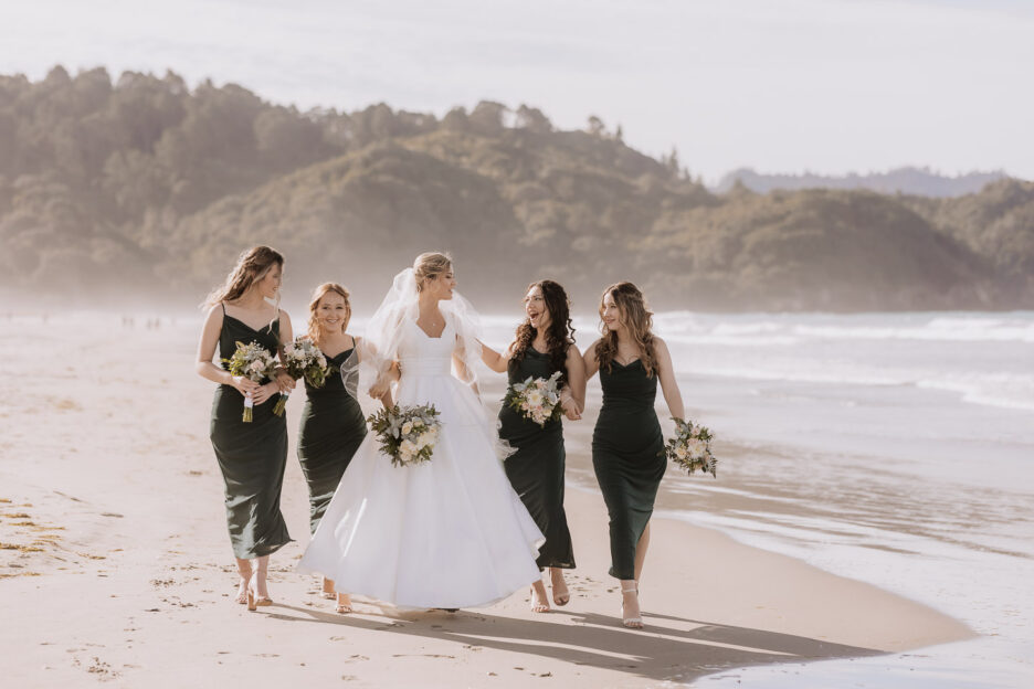 bride with her bridesmaids in green dresses walking waihi beach in front of flat white cafe