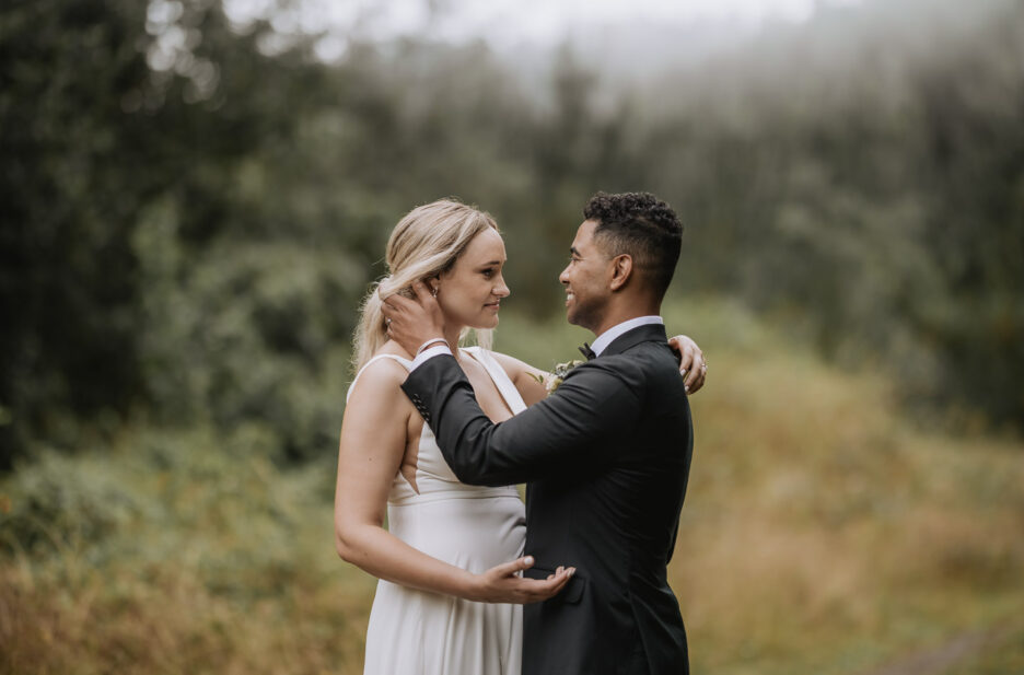 groom pushes hair from brides face in country forest scene